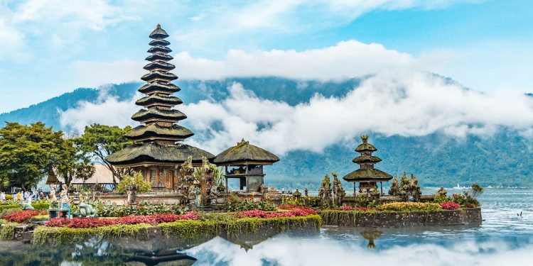 brown and green temple near body of water under blue and white cloudy sky during daytime