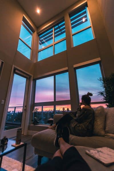 une femme assise sur son canapé dans son salon avec de grandes baies vitrées